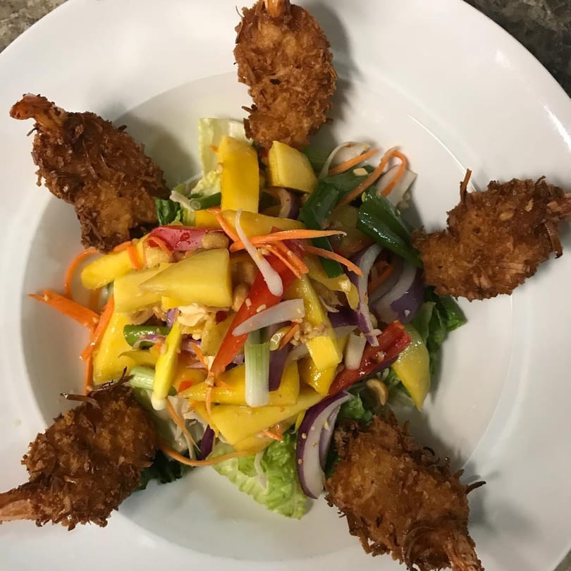 Five crispy coconut shrimp surround a vibrant Thai mango salad with mixed vegetables.