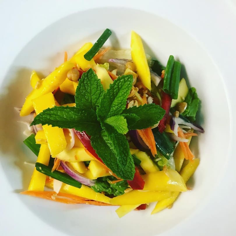 Vibrant Thai mango salad with fresh mint, red onion, carrots, and green onions in a white bowl.