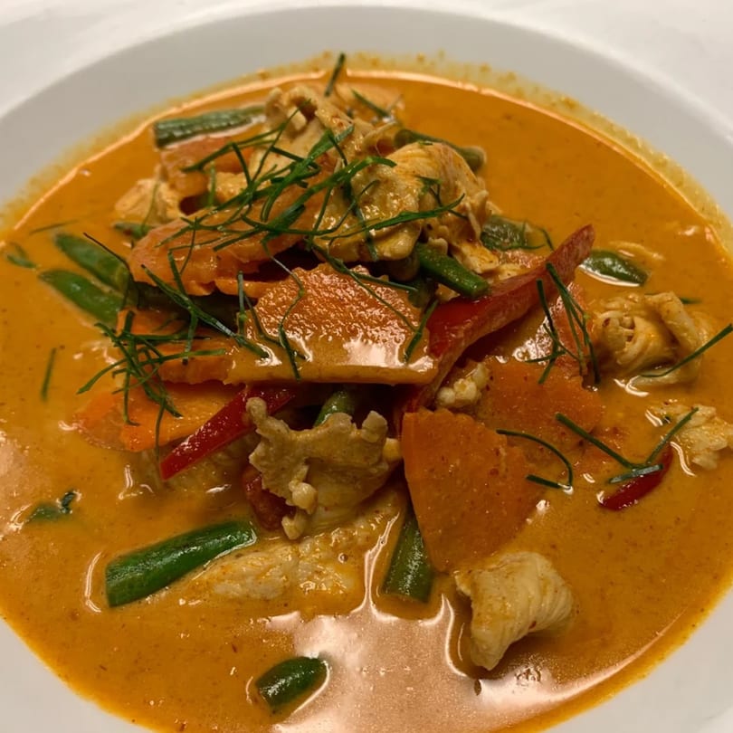 Lotus Thai Cuisine's red curry with chicken, green beans, carrots, and red peppers, garnished with herbs.