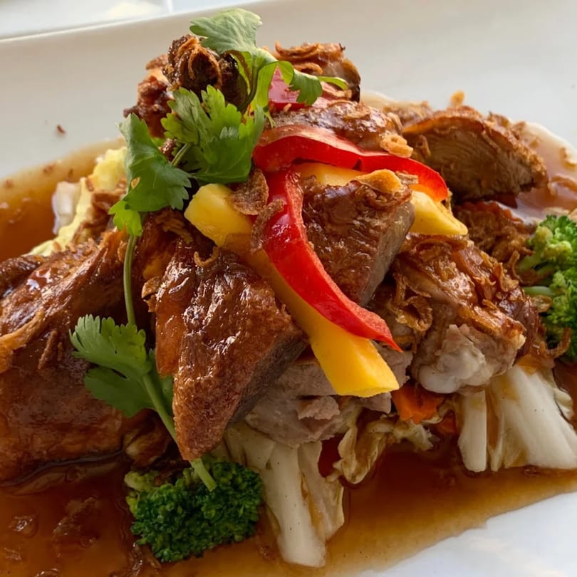 Crispy duck with red and yellow bell peppers, broccoli, and cilantro on a white plate.